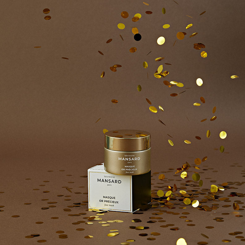 Mansard Paris 'Mange de Peau' face cream jar and its packaging box, styled with scattered gold confetti on a warm brown background.