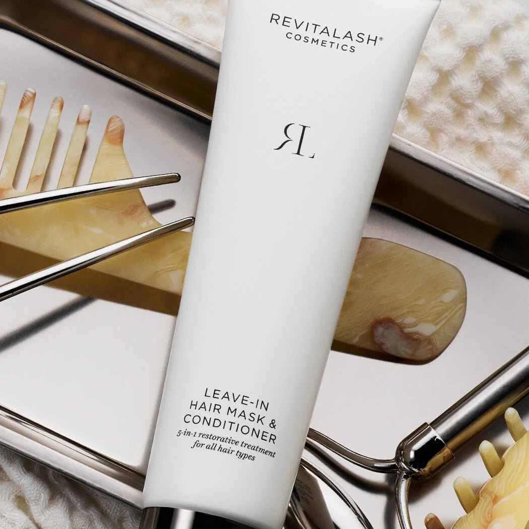 Revitalash leave-in hair mask and conditioner bottle on a decorative tray with gold tools.